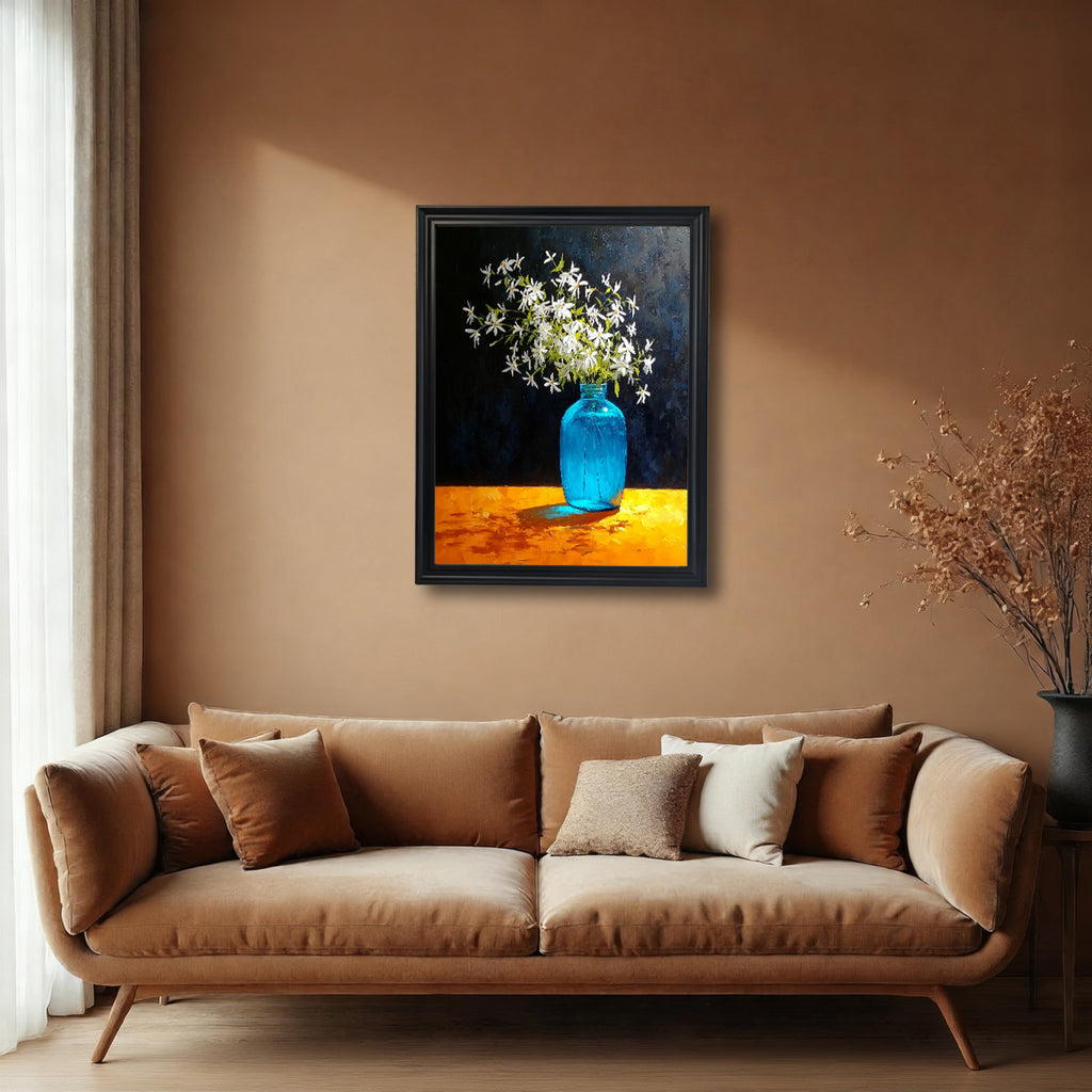 A black-framed art print hanging on a warm terracotta-colored wall above a brown velvet sofa. The painting shows a bright blue vase of white flowers on a glowing orange table.
