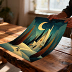 Unframed print of the whimsical snowy night painting being held and slightly curved by a person's hands over a rustic wooden table.