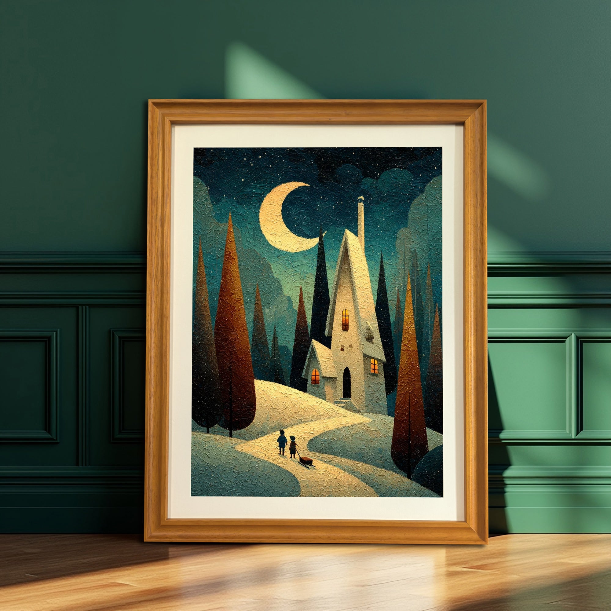 Whimsical snowy night landscape art print featuring a house, trees, and moon, in a natural wood frame, leaning on a wooden floor against a dark green paneled wall.