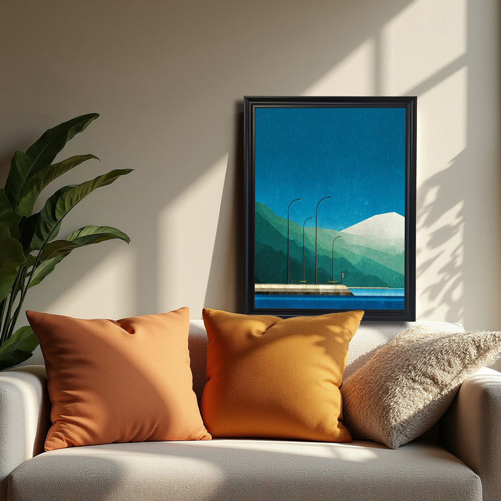 Minimalist geometric art print featuring blue water, teal and green layered mountains, a snow-capped peak, and three streetlights on a pier, in a black frame, hanging above a white sofa with orange pillows.