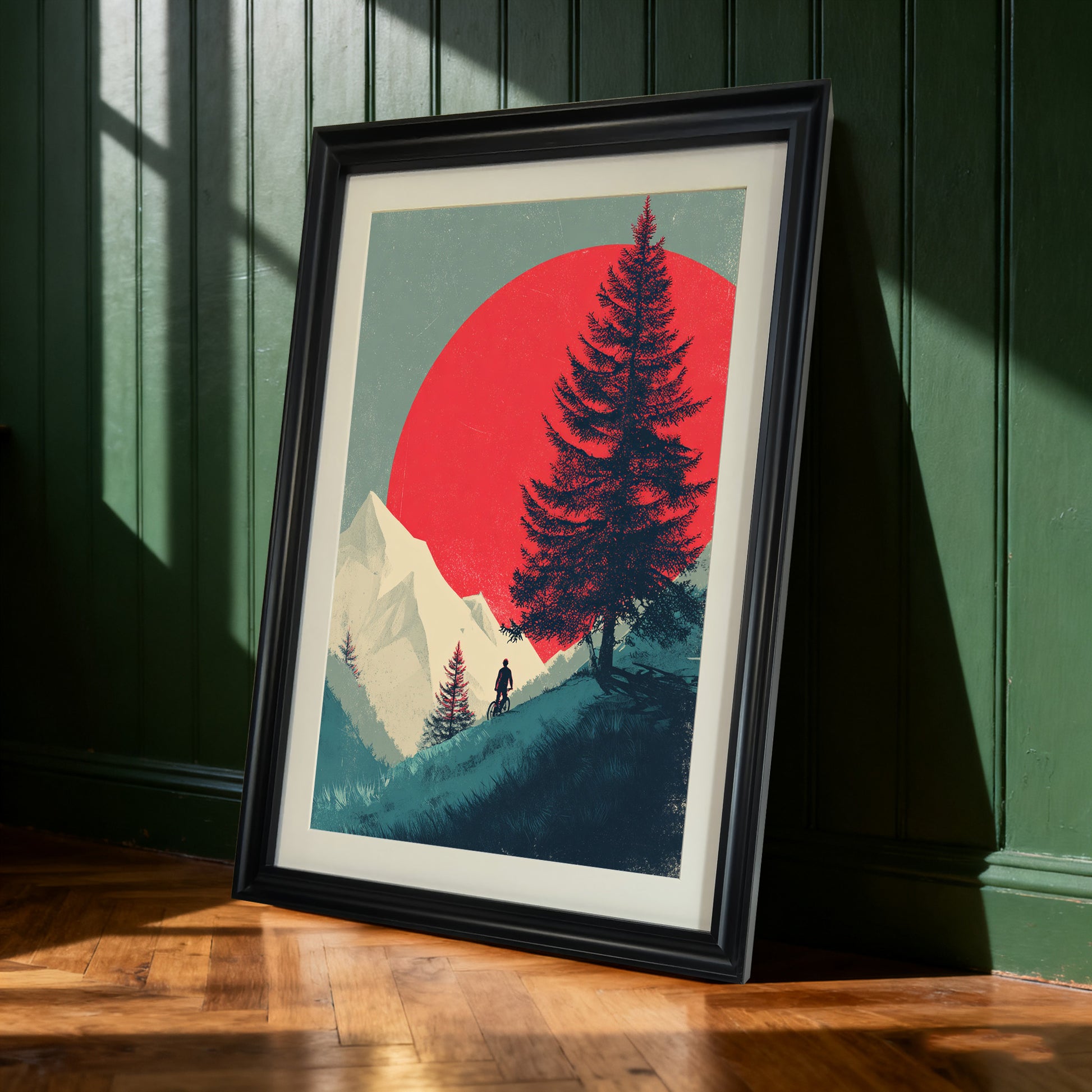 Black-framed art print of a mountain biker and red sun design, leaning against a dark green paneled wall. Sunlight casts dramatic shadows on the wooden floor.