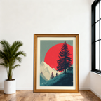 Large, natural wood-framed art print depicting a mountain scene with a red sun and a biker, leaning against a white wall next to a potted palm plant and a large window.