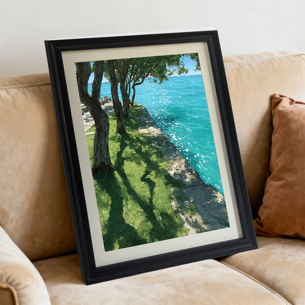 A black-framed art print resting diagonally on a tan, plush sofa next to a brown pillow. The artwork features trees casting shadows on green grass by bright, sparkling blue water.