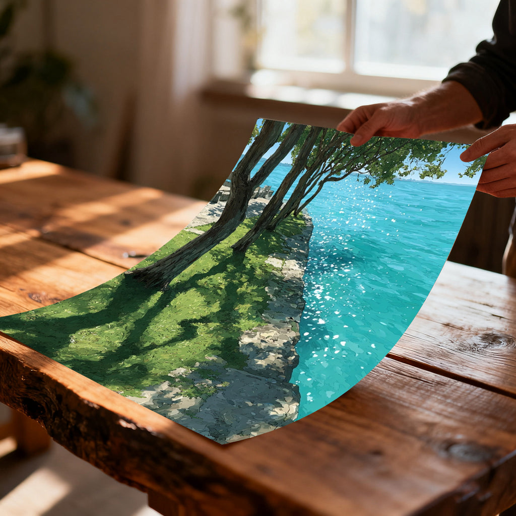 Close-up of hands holding a glossy art print (unframed) of trees, grass, and sparkling turquoise water, curving slightly over a rustic wooden table.