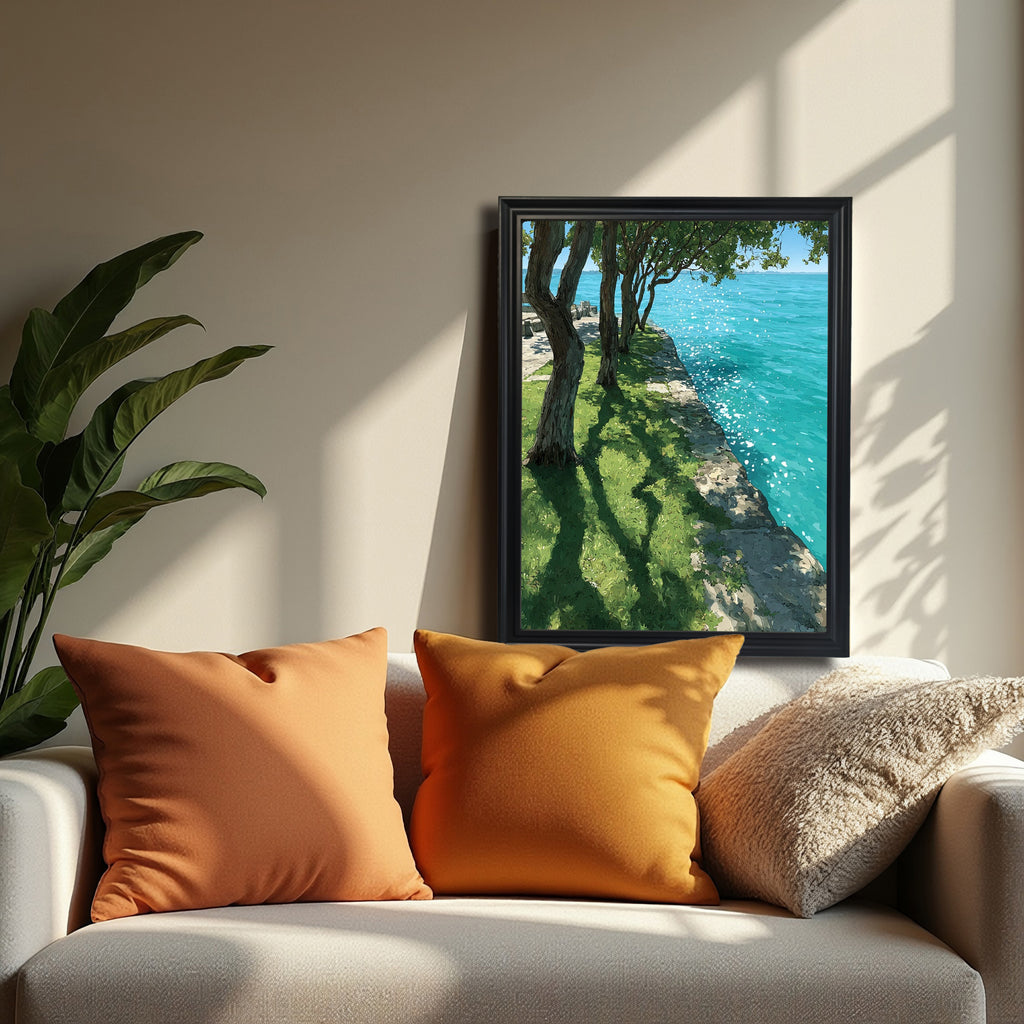 A black-framed art print standing on a white sofa with two orange pillows. A large green plant is on the left. The print shows a sunny park scene next to vibrant blue water.