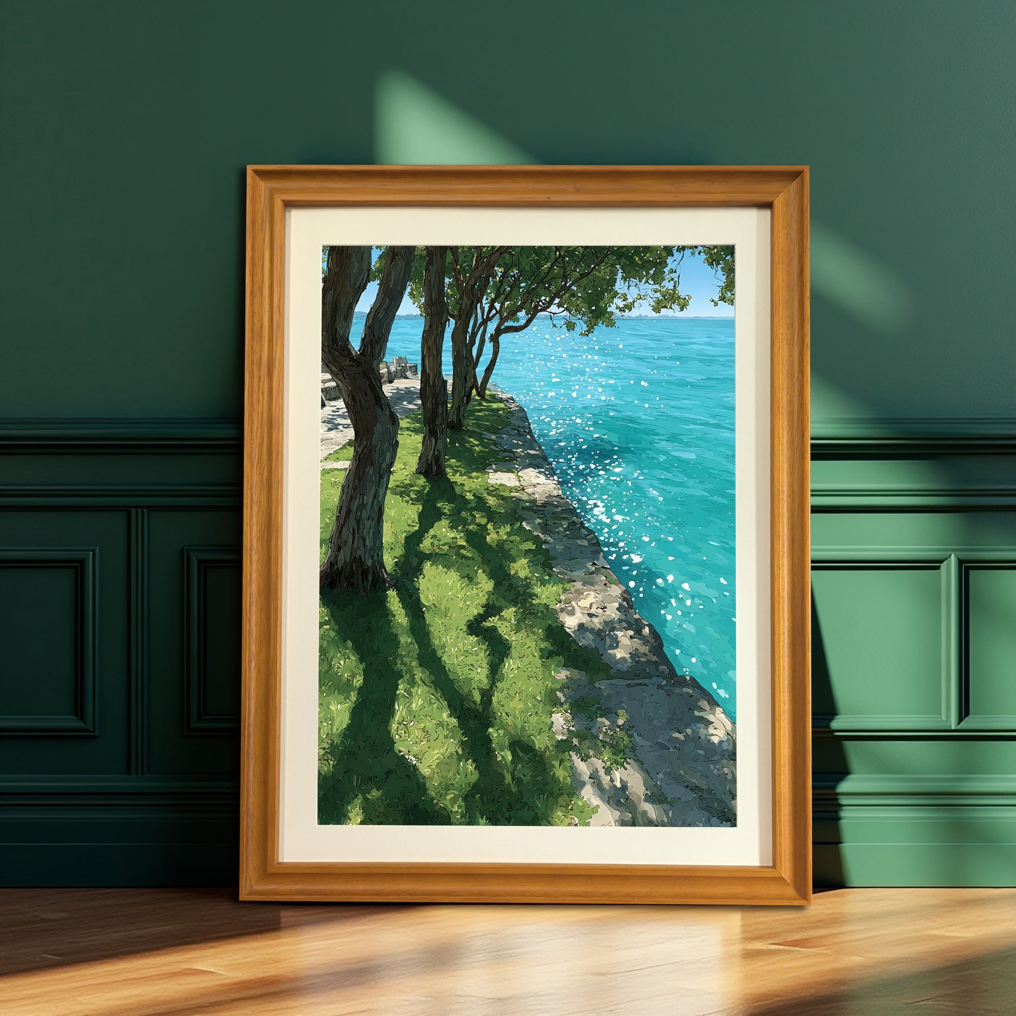 A vertical wood-framed art print leaning against a dark teal, paneled wall. The artwork depicts a sunny scene with trees casting long shadows on green grass next to bright turquoise water.