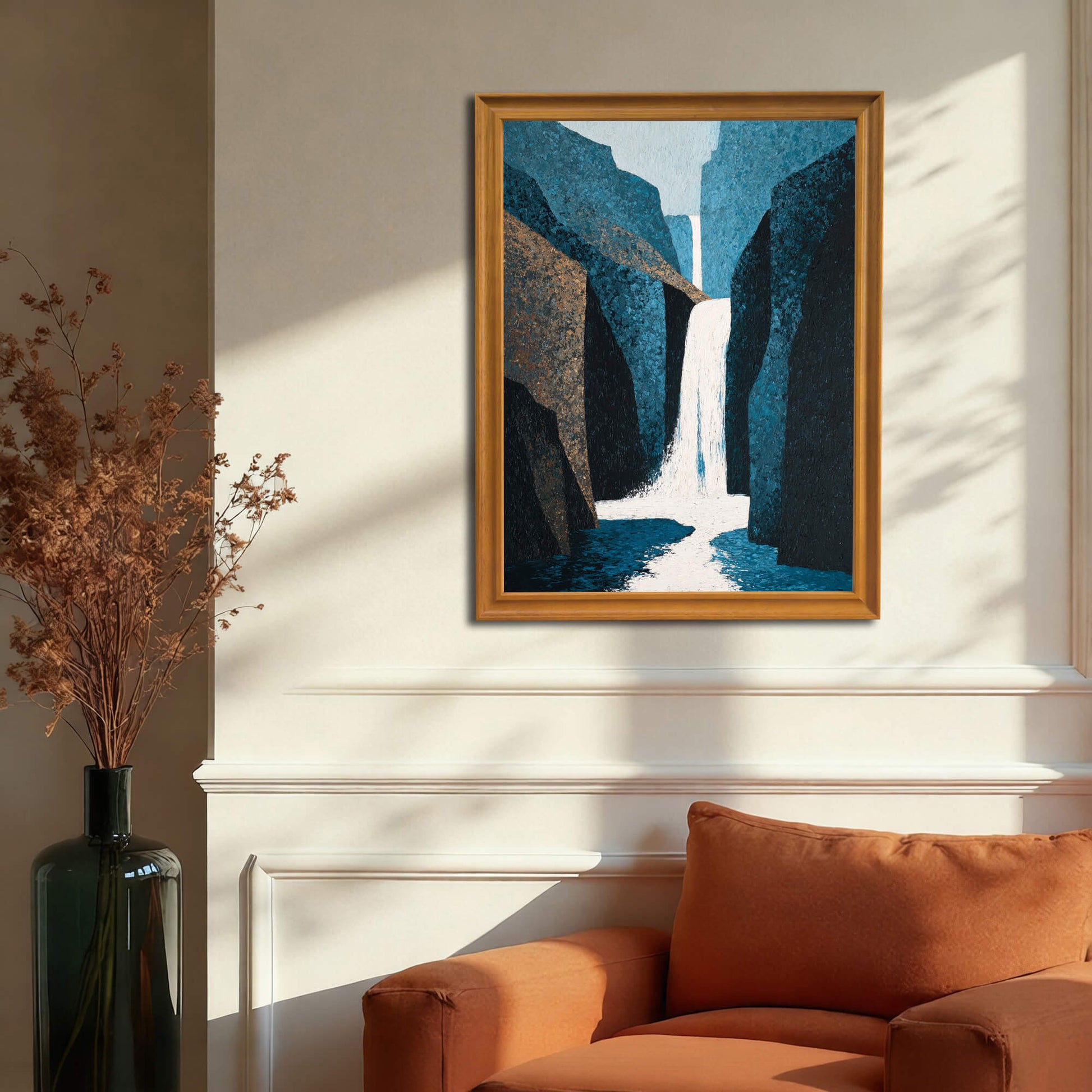 Abstract waterfall art print in a gold or dark natural wood frame hanging above an orange armchair and white wainscoting, illustrating a cozy, warm living room decor.