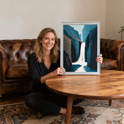 Smiling woman sitting on the floor holding the abstract waterfall art print in a white wood frame, providing scale and showing the artwork's size relative to a person.
