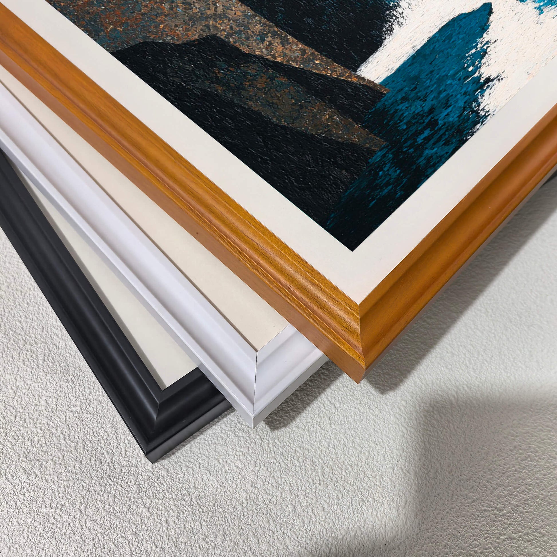 Stacked close-up of different wood frame options for art prints: black, white, and natural light wood (oak/maple). Shows the frame molding detail and finish.