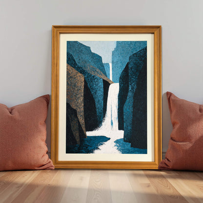 Abstract waterfall art print in a natural light wood frame (oak/maple), leaning against a gray wall on the floor between two terracotta-colored pillows, demonstrating lifestyle decor.