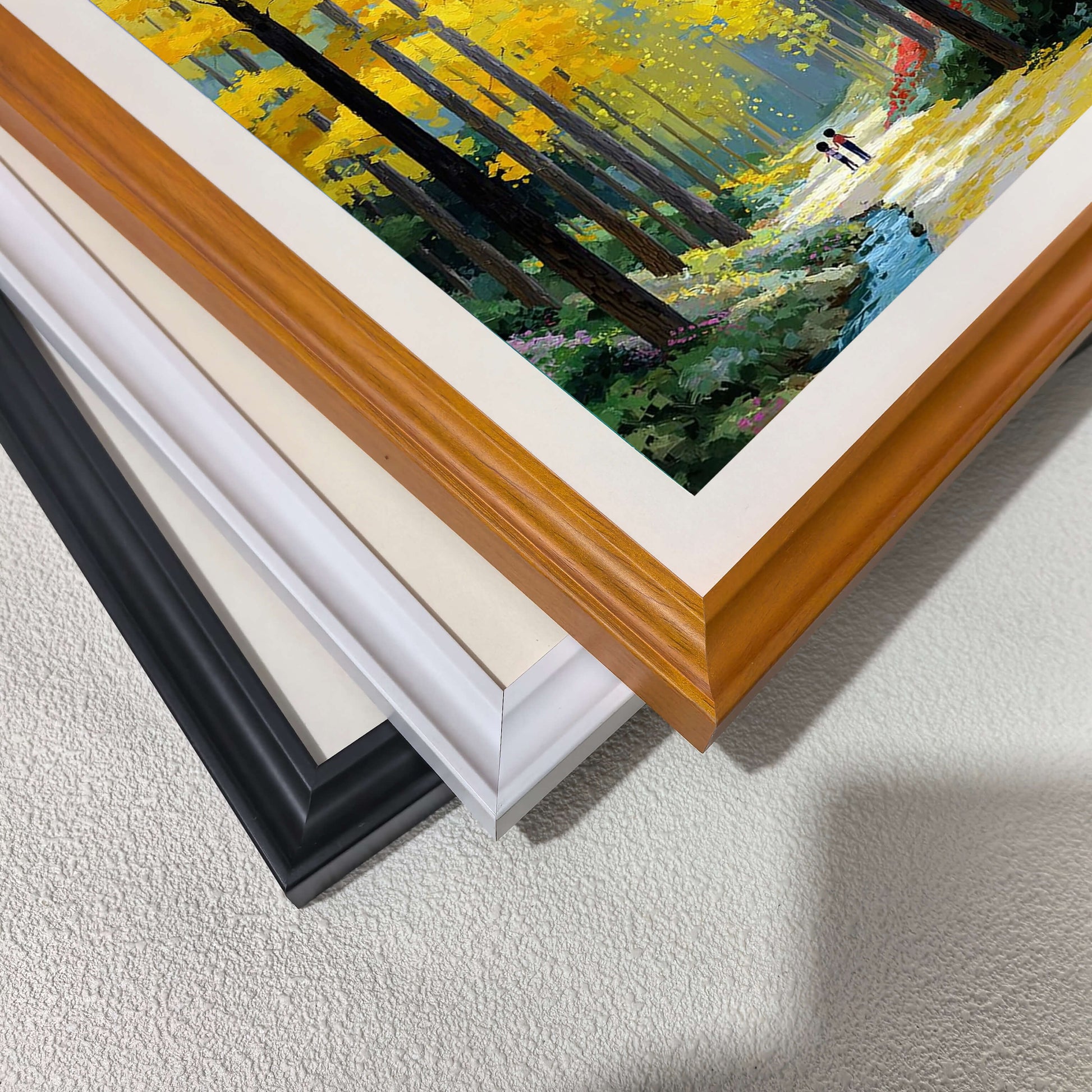 A close-up, angled shot of three stacked picture frames (black, white, and wood) showing the corner detail of the forest artwork.