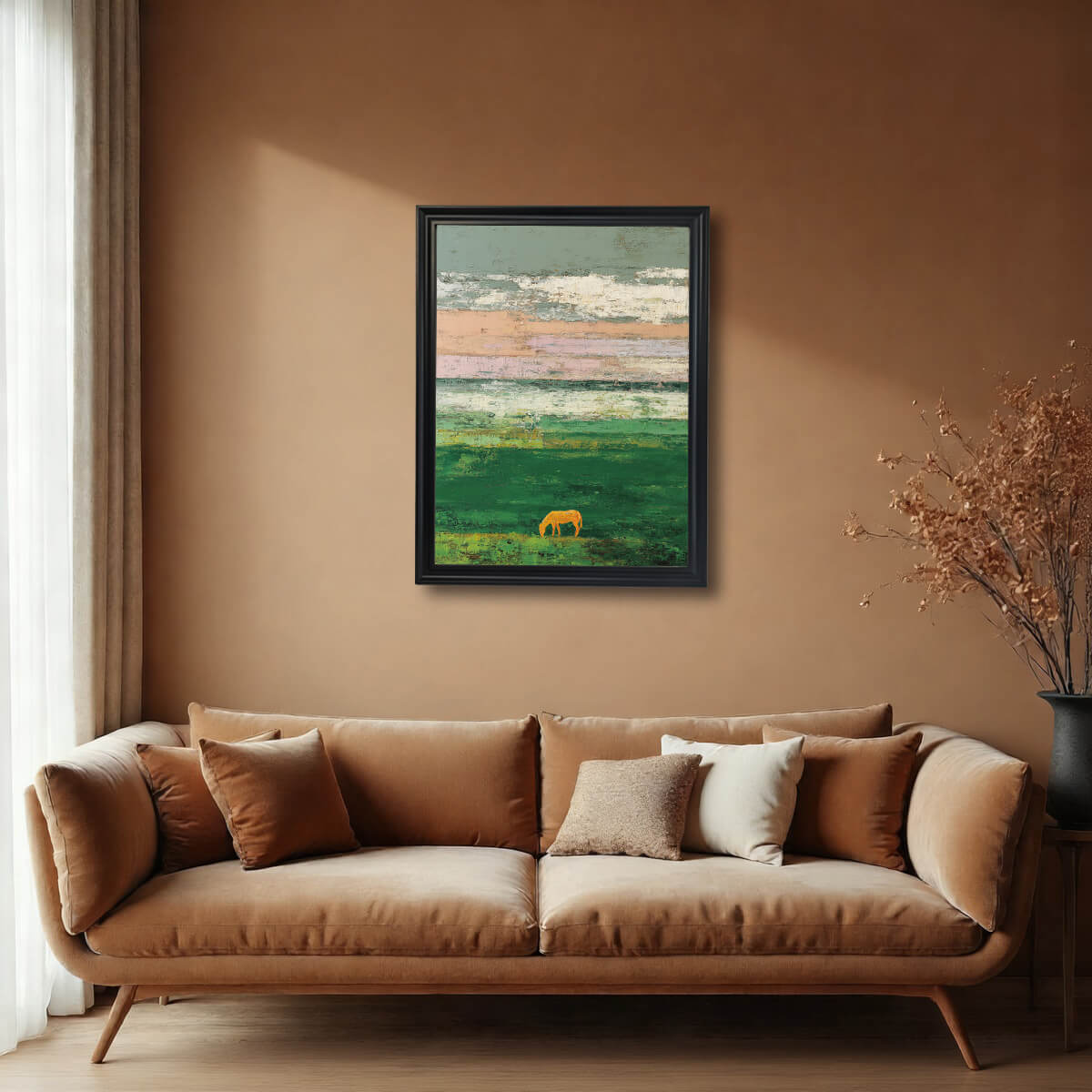 A framed art print of an abstract field with a golden horse silhouette, with a textured sky of pale colors, hanging above a tan velvet sofa in a room with warm, earthy brown walls. The frame is black.