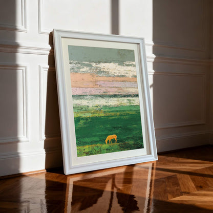 A framed art print of an abstract landscape with a golden horse silhouette, leaning against a white wainscoted wall on a glossy hardwood floor, brightly lit by sunlight. The frame is white.