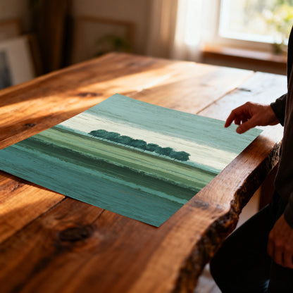 Overhead shot of a hand touching an unframed art print depicting a horizontal row of trees over banded, abstract green and teal fields, lying on a rustic, live-edge wood table.