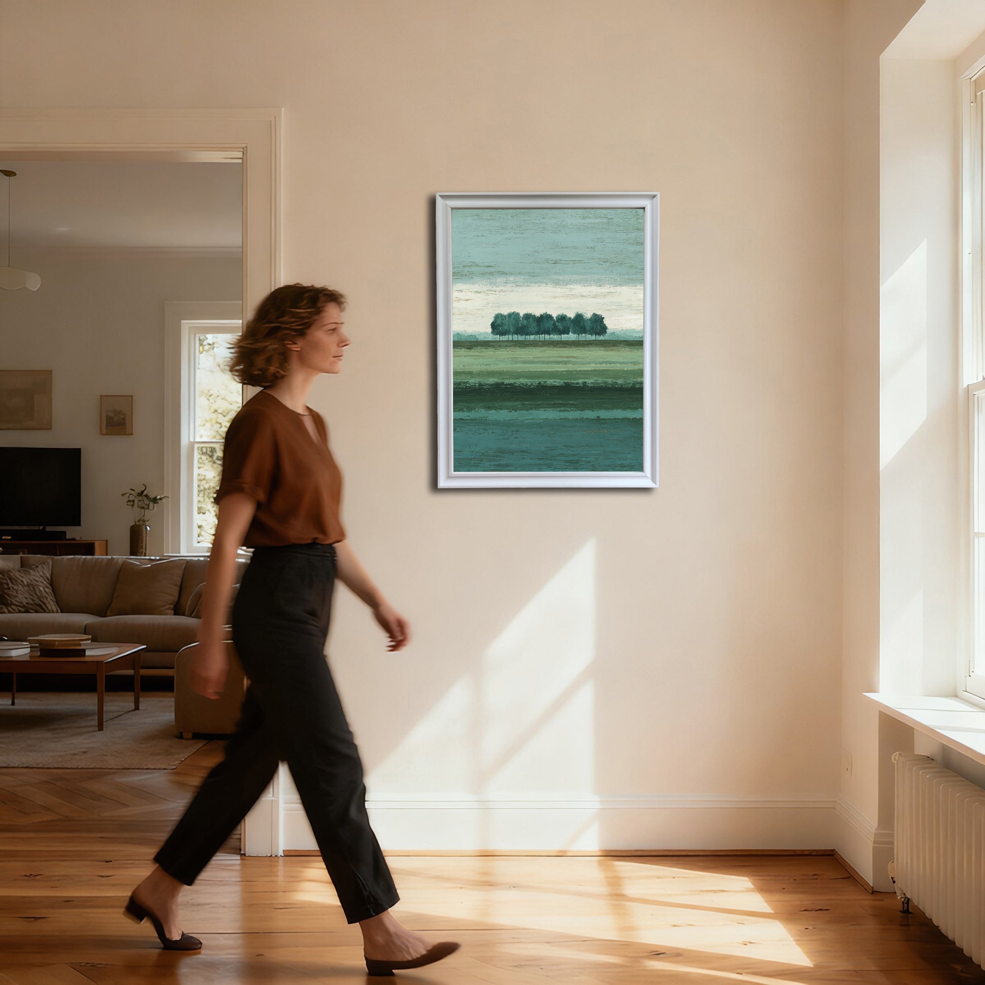 Full-body shot of a woman walking past a vertical abstract landscape art print (row of trees) in a thin white frame, hanging on a cream wall in a brightly lit hallway.