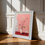 A vertical, framed painting of white lotus flowers in a white vase against a pink and red background. The painting is in a thick white frame and is leaning against a white wainscoted wall on a wooden floor, with sunlight casting sharp shadows.