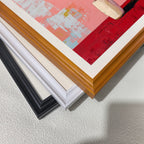 A close-up, stacked view of the corners of three different wooden picture frames: black, white, , and light brown (wood grain), showing the frame profiles and the edge of the painting."