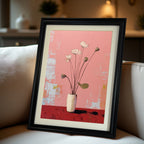A close-up, angled view of a vertical, black-framed painting of white lotus flowers on a pink and red background with a white mat, resting on a beige sofa.