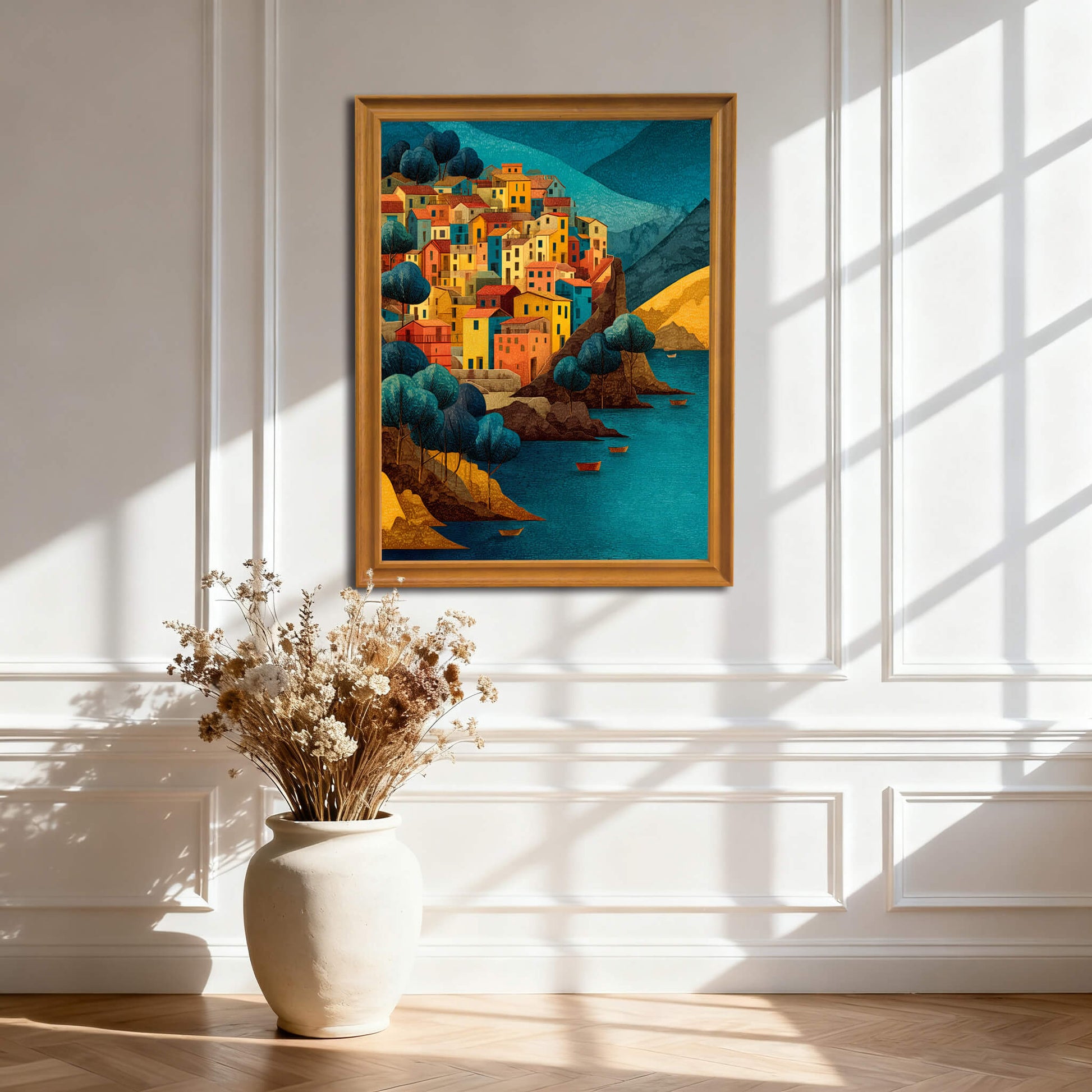 Art print of a colorful coastal town in a light wood (natural) frame, hanging on a white wall with wainscoting and natural light shadows.