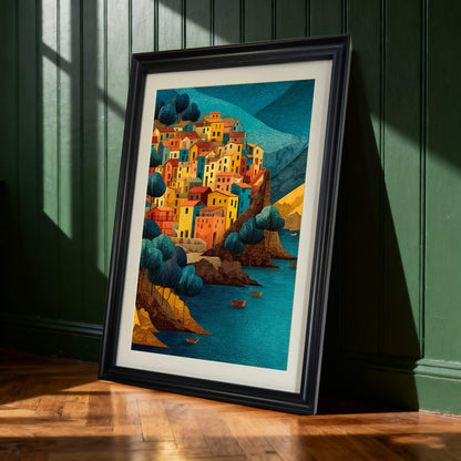 Art print of a colorful cliffside village in a black frame, leaning on a wooden floor against a dark green paneled wall.