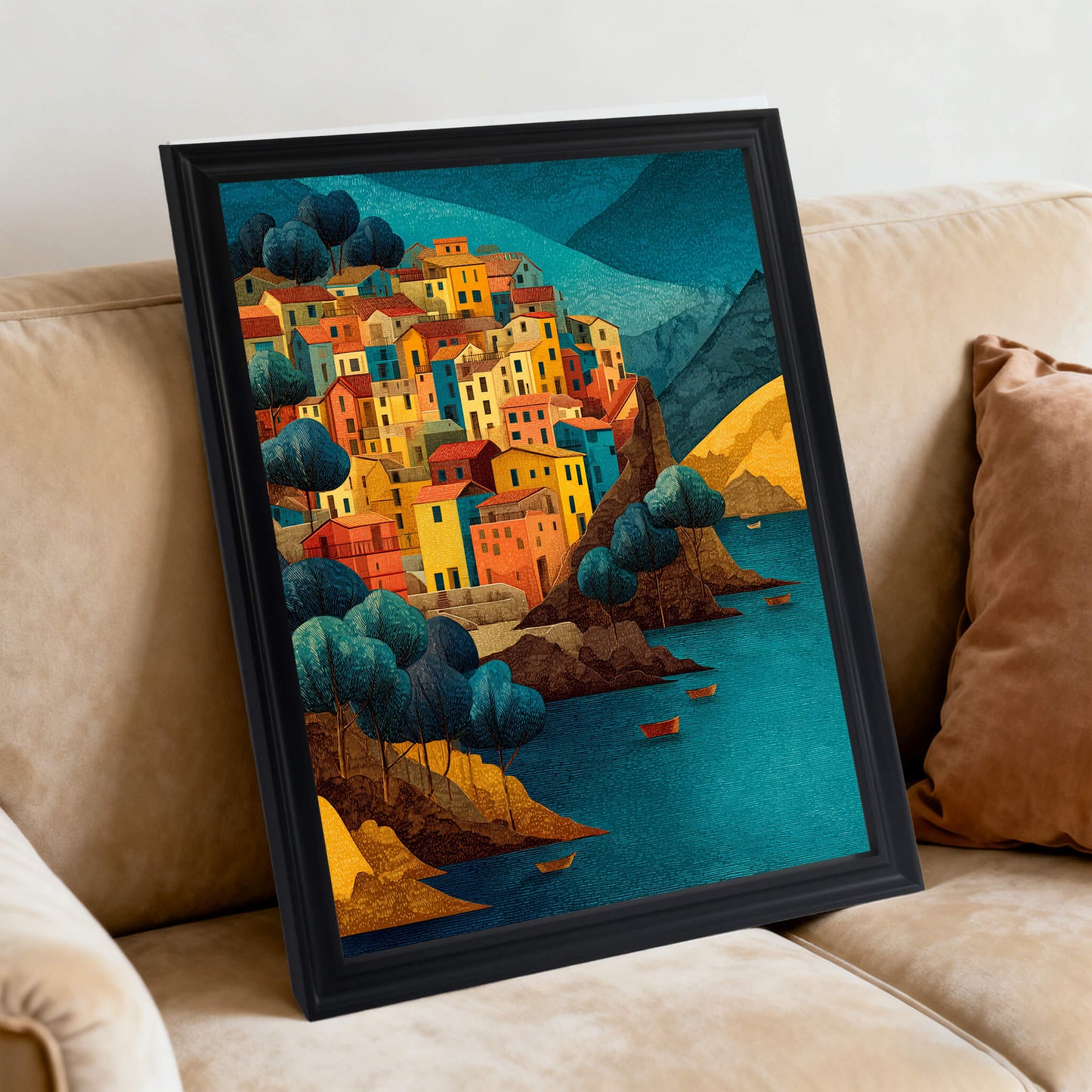 Art print of an Italian town overlooking the water in a black frame, leaning against a beige couch cushion.