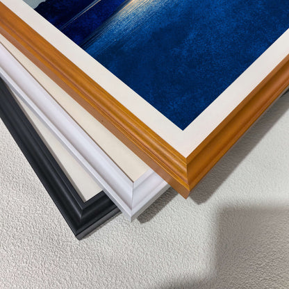 Stacked close-up view of the three  different wood frame options: black, white, and dark wood (brown/natural), with a corner of the blue art print visible.