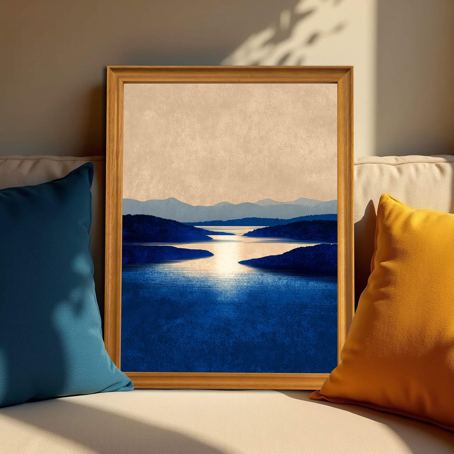 Framed art print of a dramatic blue water landscape in a light wood (natural) frame, resting on a beige sofa between a blue and a yellow pillow.