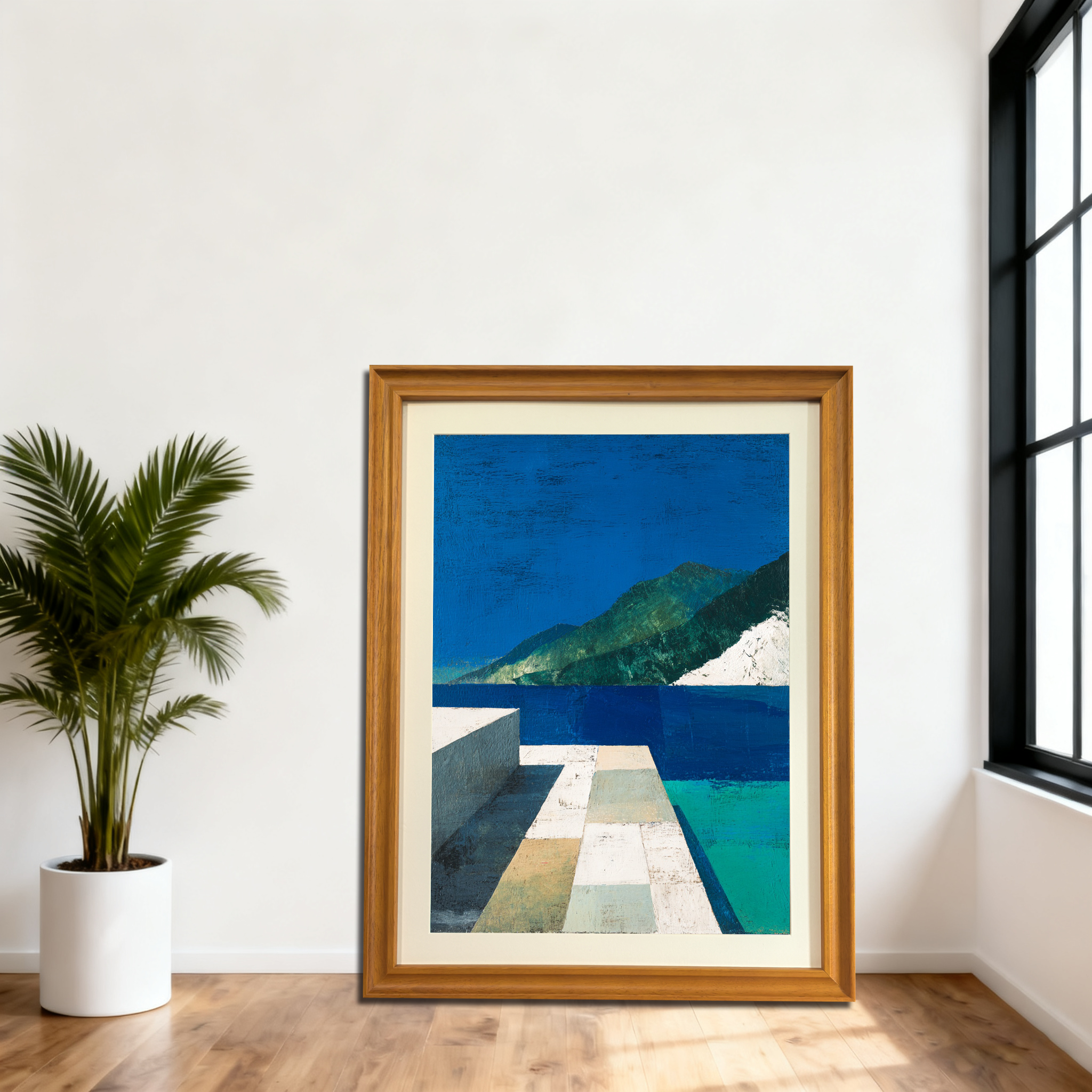 Large, natural wood-framed abstract landscape art print leaning on the floor against a white wall in a modern room with a large black window and a potted palm."