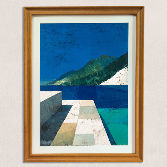 Close-up view of an abstract landscape art print, framed in natural wood, against a neutral-colored wall. The print features a vibrant blue sky, dark green mountains, and geometric white/tan foreground elements.