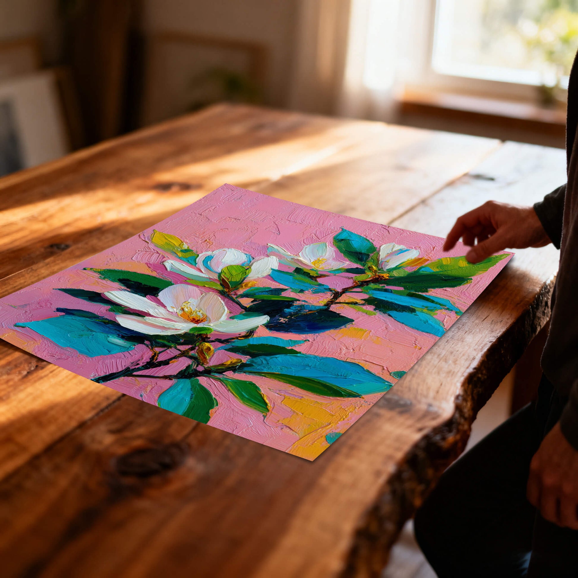 Perspective view of an unframed magnolia art print laying on a rustic wooden table in natural sunlight.