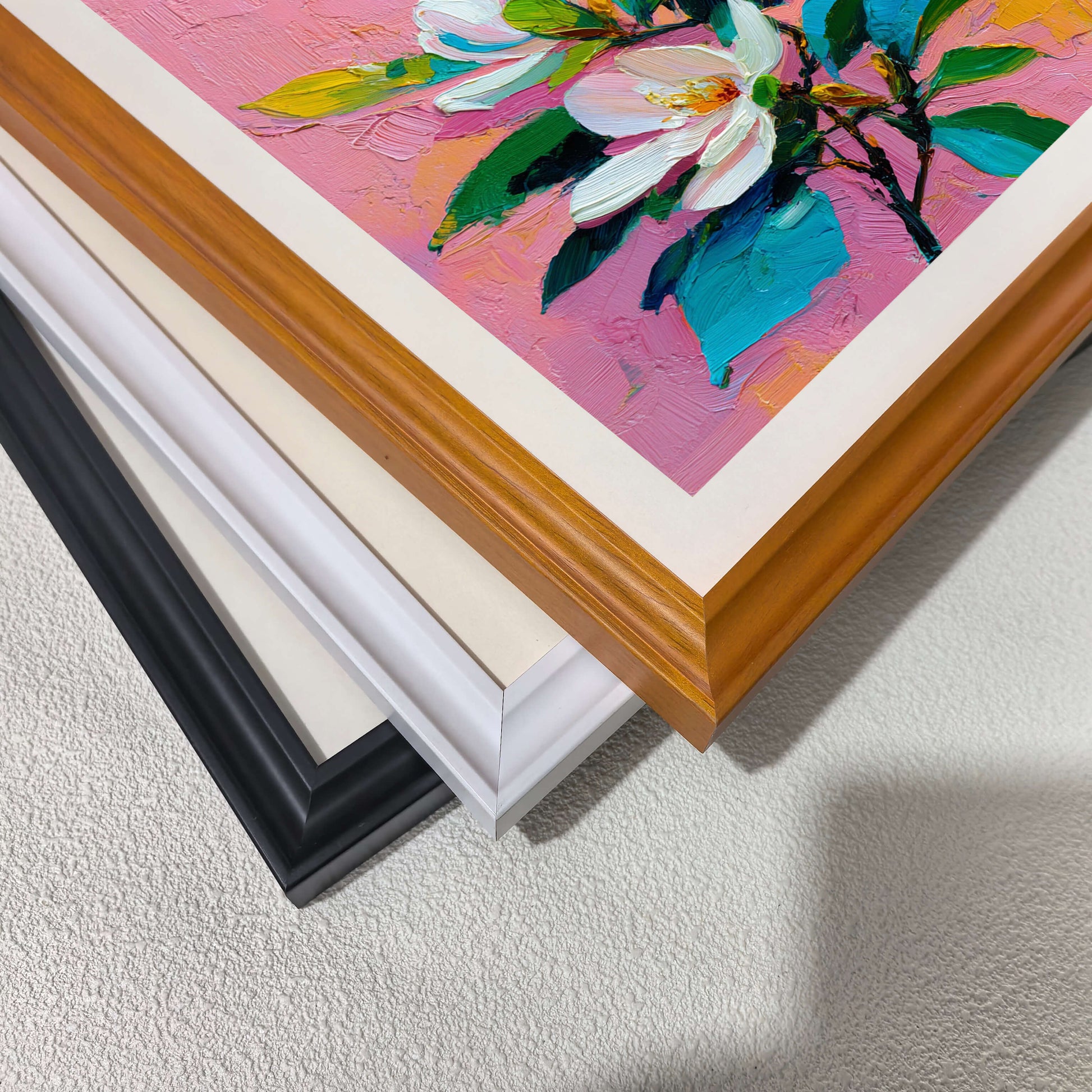 Close-up view of three different frame options (wood, white, and black) for the magnolia floral print.