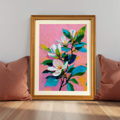 Wood-framed floral art print of white magnolias on pink, placed on a floor between two brown pillows.