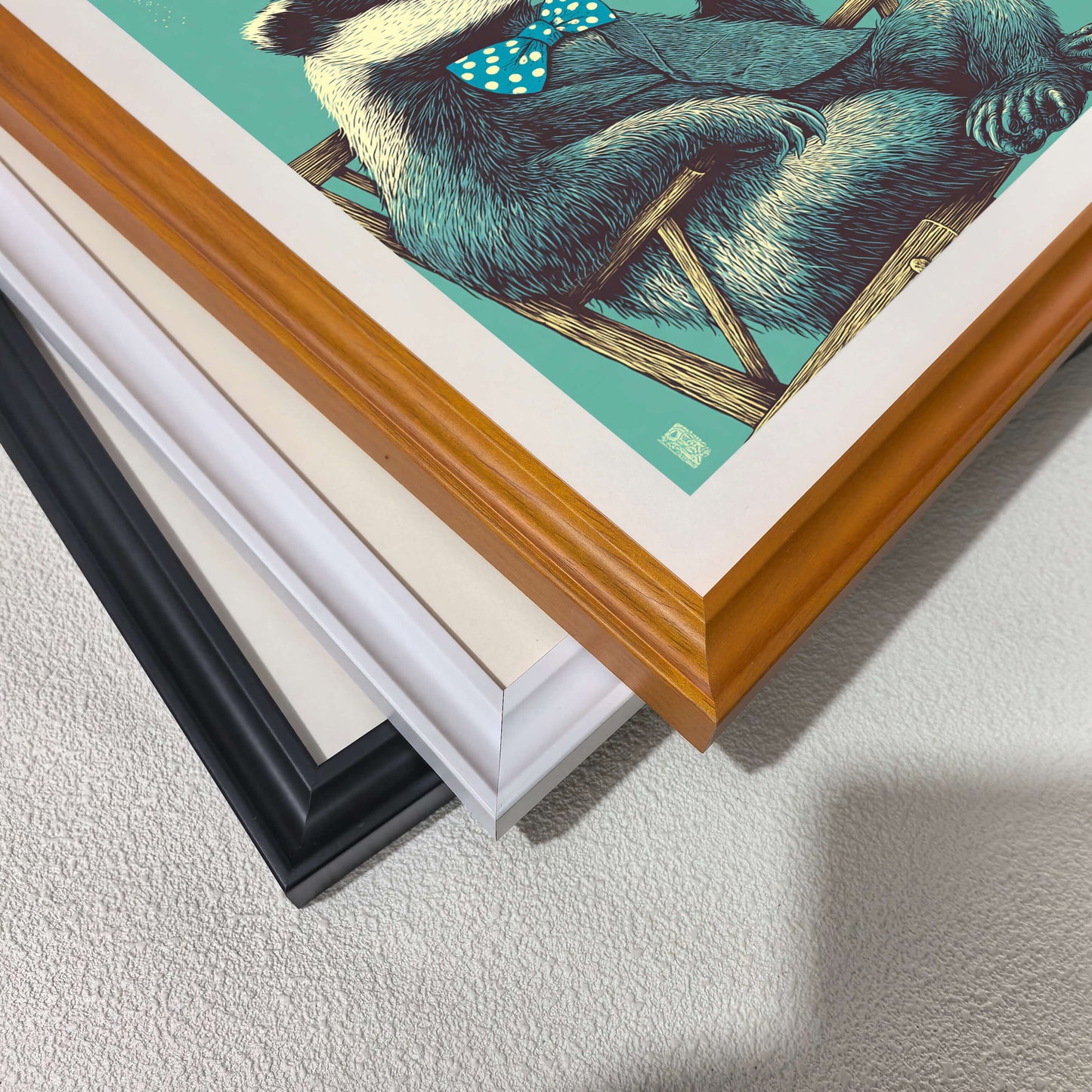 Detail shot of stacked art frames in black, white, and natural wood finishes featuring a blue badger print for customizable framing options.