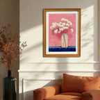 The art print, in a natural wood/gold frame, hangs on a cream-colored wall above an orange armchair in a sunlit room, showcasing the artwork's scale in a cozy home setting.
