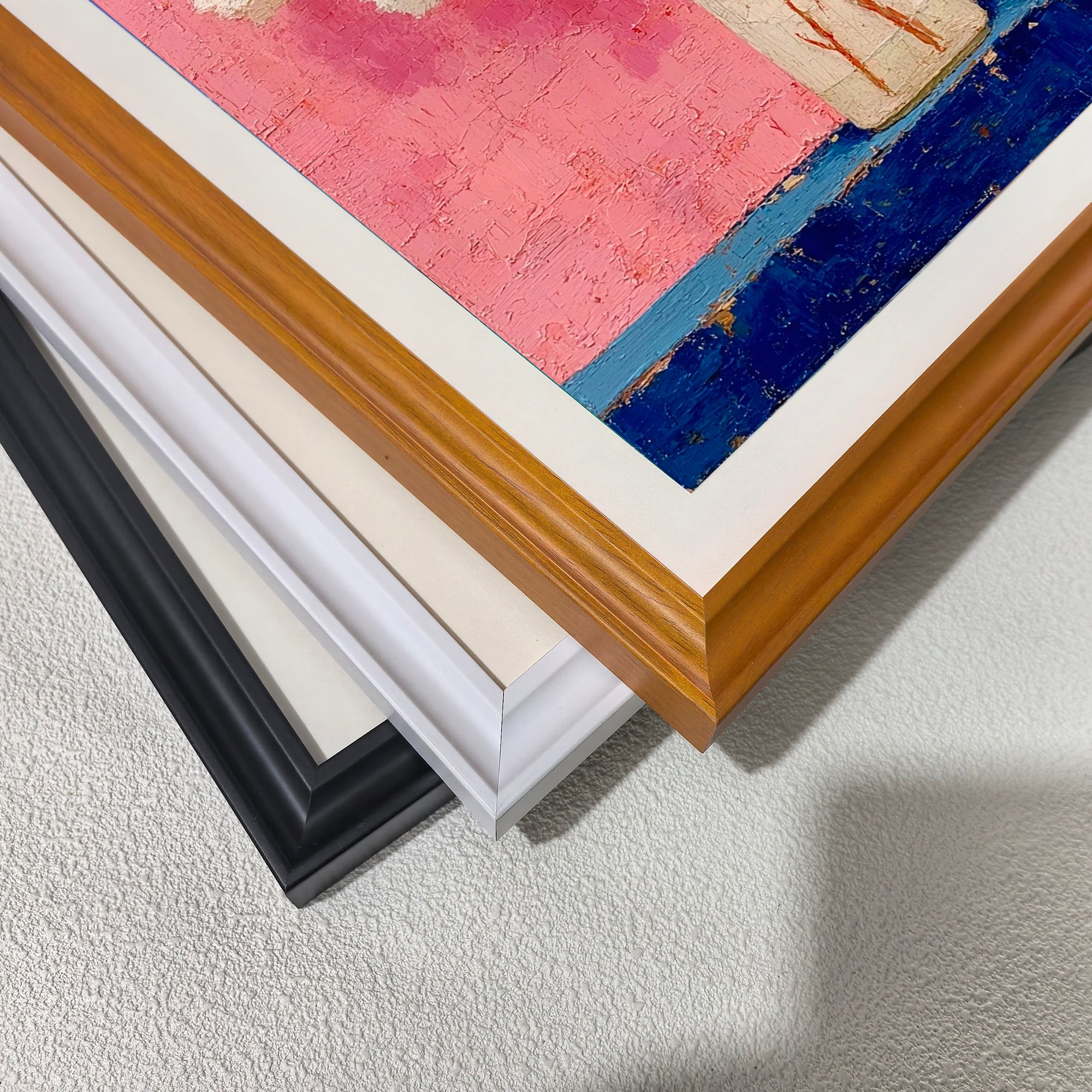 A close-up, stacked view of the corner of the art print, showing three different frame options: black, white, and orange color frame.