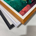 Close-up of three stacked wood picture frame corners in black, white, and natural brown, showing the art print inside which features dark green and red colors.