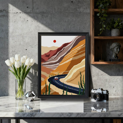 The desert road illustration framed in black wood, sitting on a marble countertop next to a vase of white tulips and a vintage camera, against a modern concrete wall.