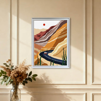 The modern desert landscape art print featuring a winding road and layered rock formations, framed in white, hanging on a warm beige wall with wainscoting details, above a vase of dried pampas grass.