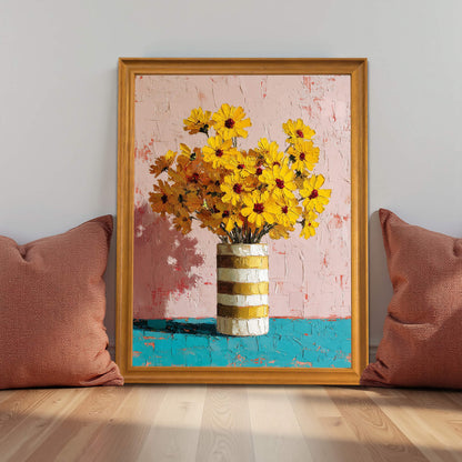 A vibrant, textured impasto oil painting of yellow sunflowers in a gold-and-white striped vase. The artwork features a soft pink background and a turquoise table, framed in a light wood frame and leaning against a wall between two terracotta-colored pillows on a hardwood floor.