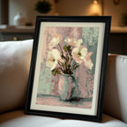 Close-up of the framed art print: white and pink flowers in a pale blue vase against a textured pastel background, set in a black frame with a mat, leaning on a light-colored sofa.