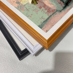 Close-up of three stacked wood picture frame corners in black, white, and natural light brown, showing the art print inside with pastel pink and green colors.