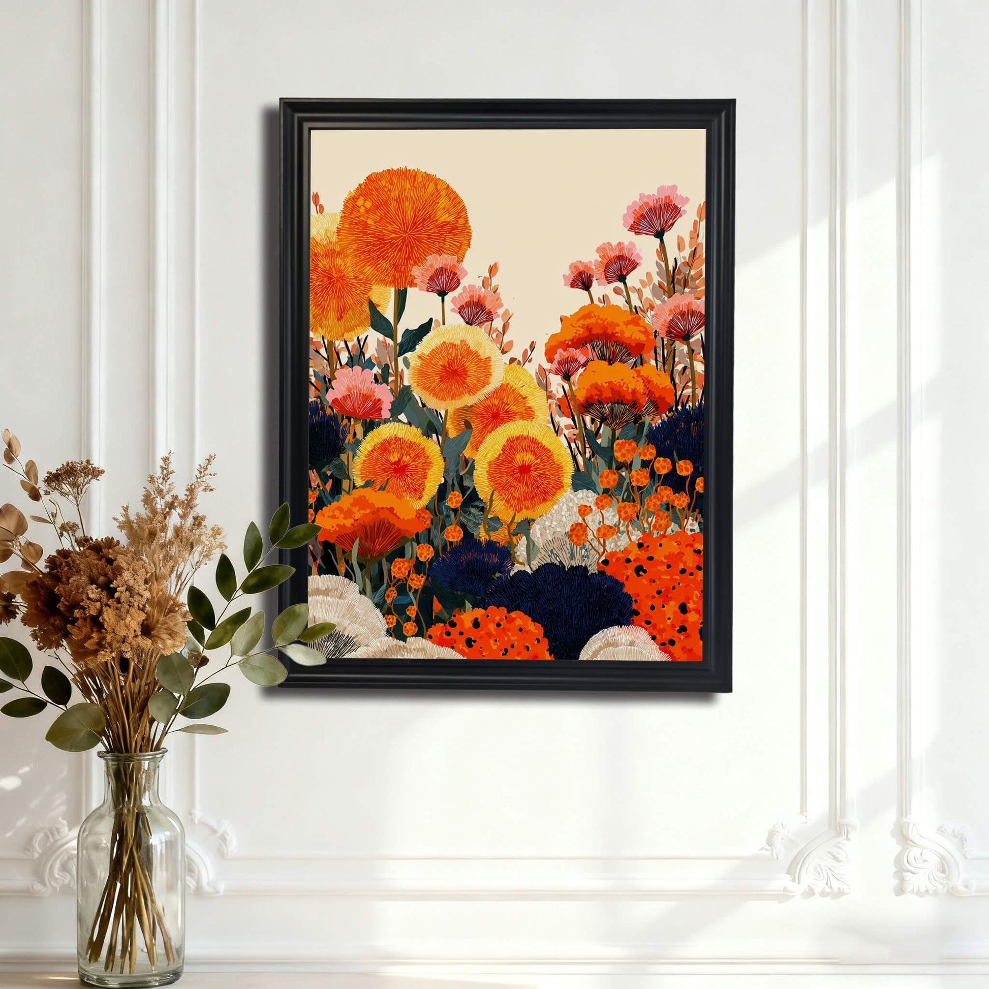 A black-framed floral art print hung on a white wall with ornate classical molding. In the foreground, a glass vase holds dried botanical stems.