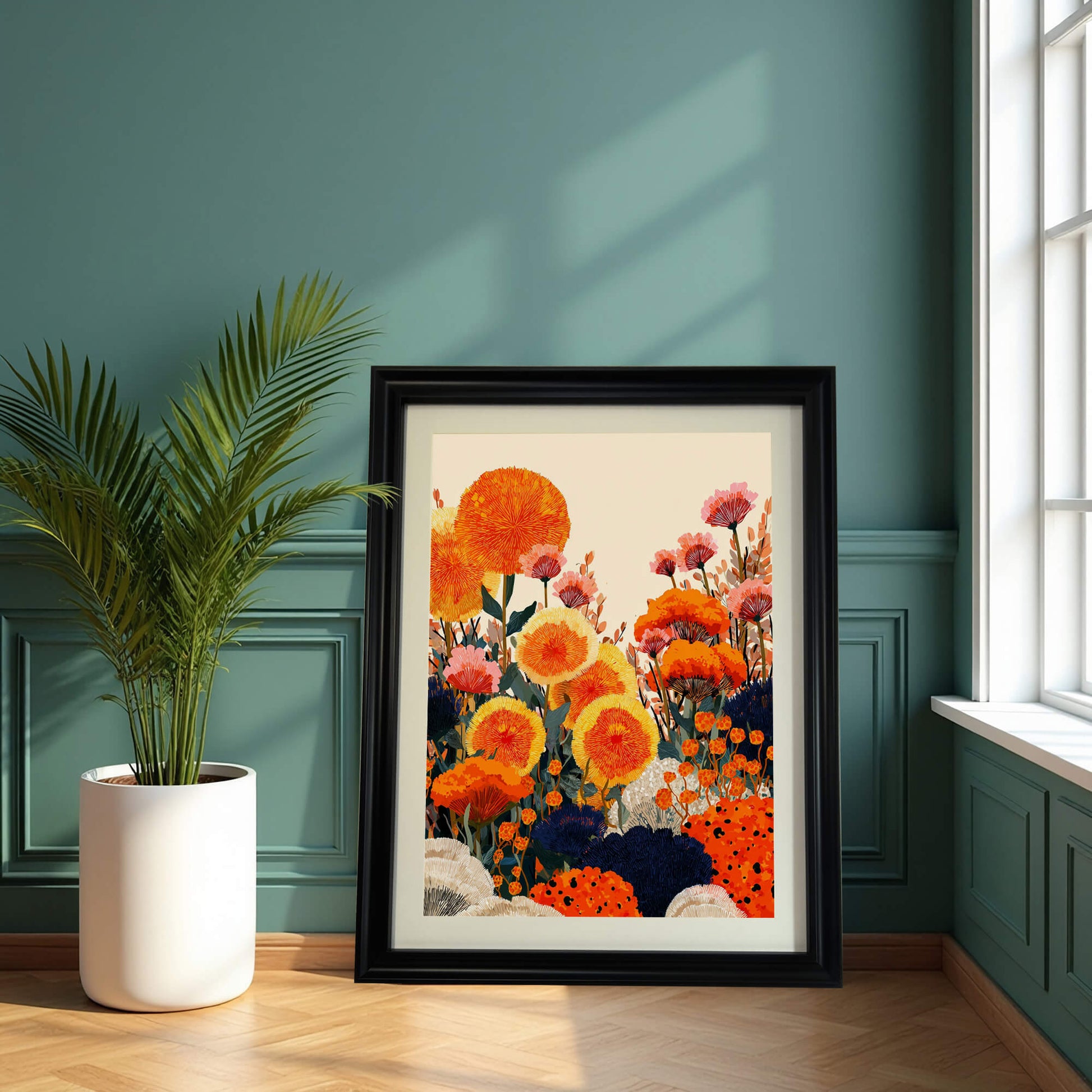  A large, black-framed floral art print leaning on a light wood floor against a teal wainscoted wall. A tall potted palm plant in a white ceramic pot sits to the left of the frame.