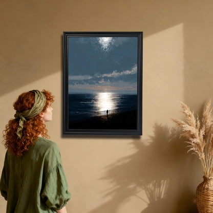 Moody ocean sunset art print in a black wood frame hanging on a tan wall. A woman with red hair and a green headscarf is admiring the piece, showing a bohemian decor style.