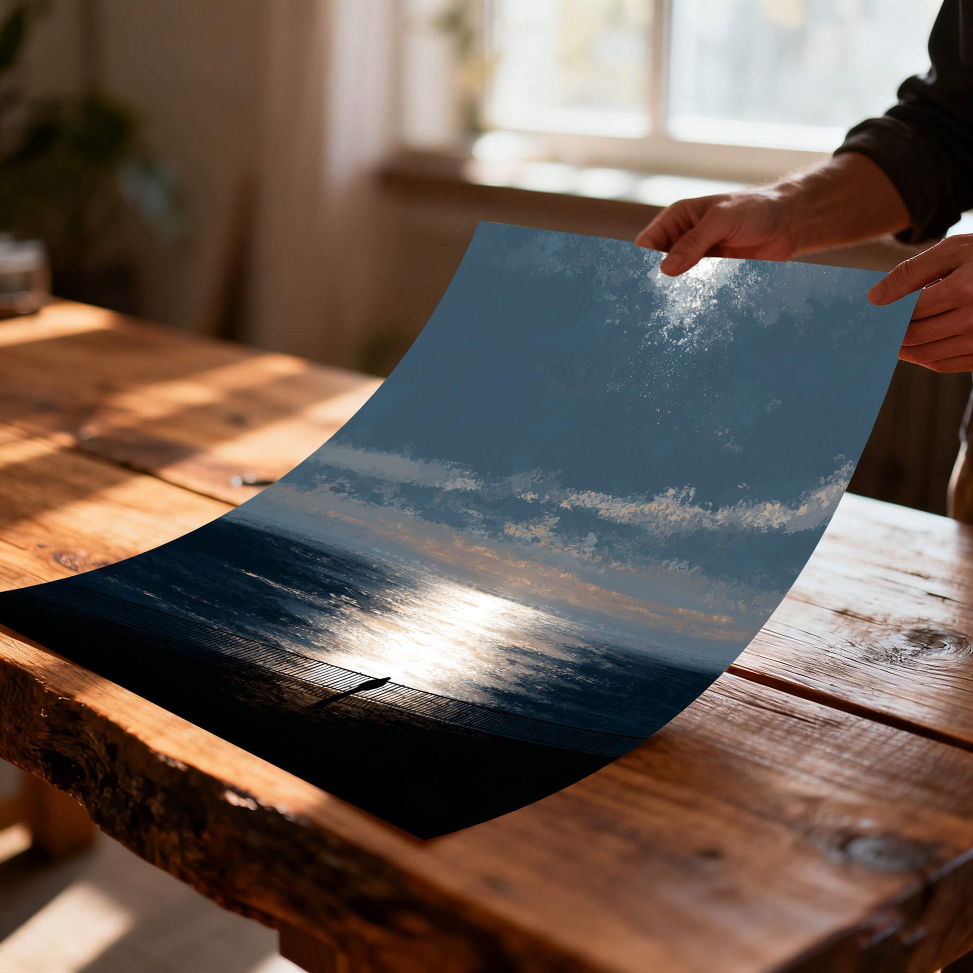 Unframed, flexible art print of the moody ocean sunset being held over a rustic wood table, illustrating the print material quality and texture.