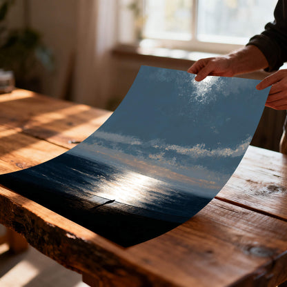Unframed, flexible art print of the moody ocean sunset being held over a rustic wood table, illustrating the print material quality and texture.
