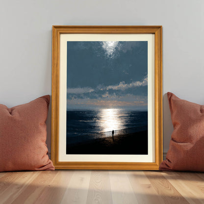 Moody ocean sunset art print in a natural light wood frame (oak/maple), leaning against a gray wall on the floor between two terracotta-colored pillows, demonstrating a cozy, grounded decor style.