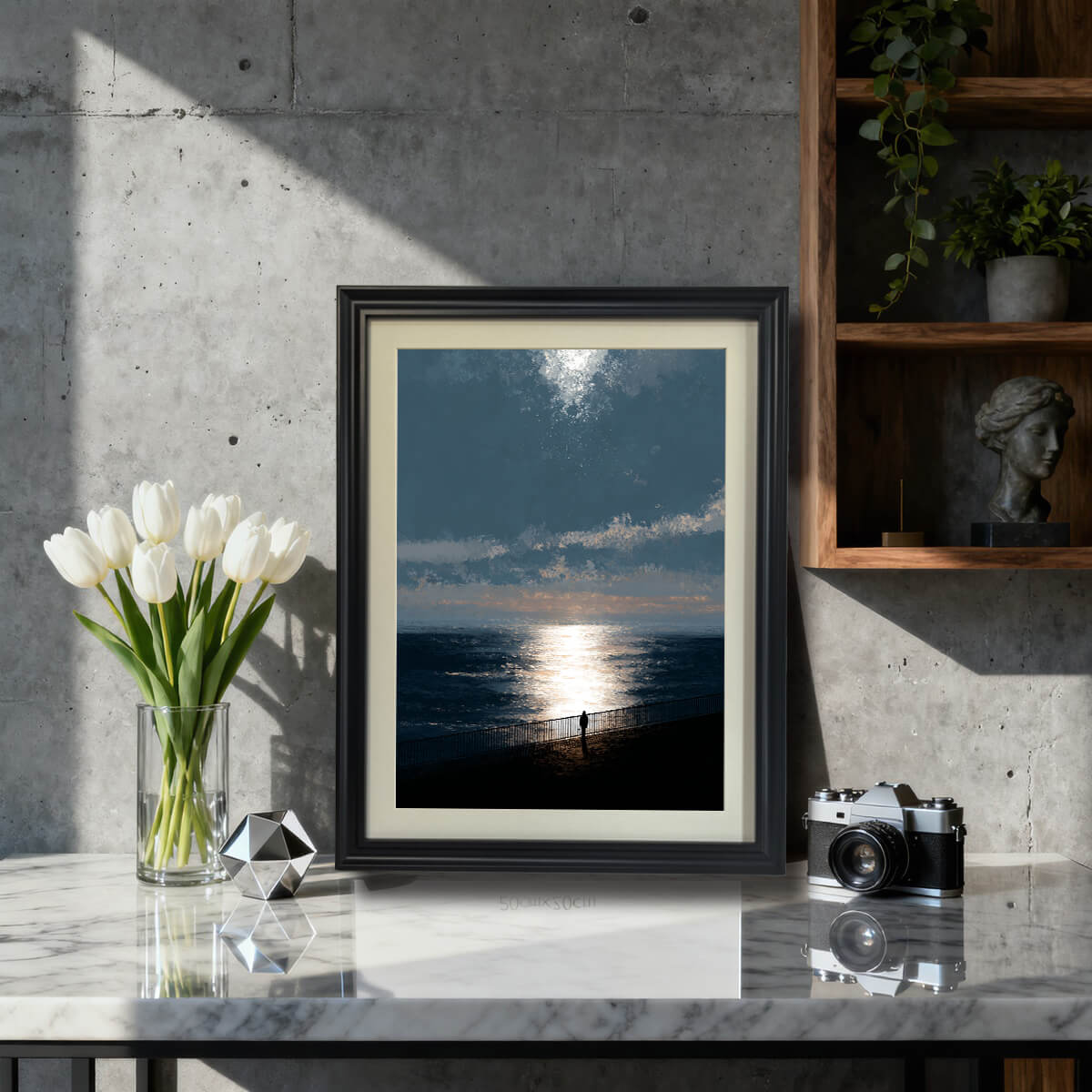 Moody ocean sunset art print in a black wood frame with a mat, sitting on a marble countertop next to white tulips and a vintage camera, styled for modern or industrial decor.