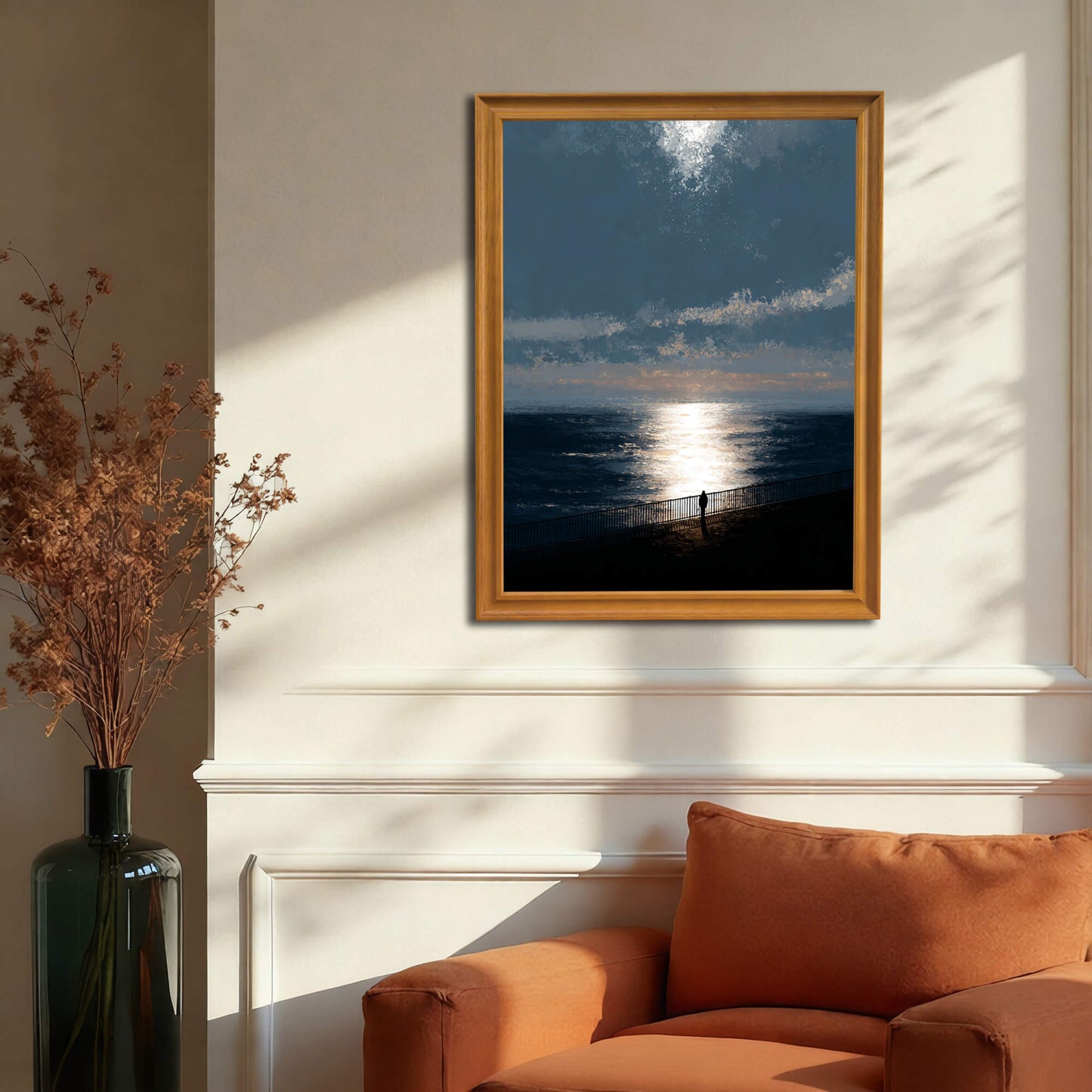Moody ocean sunset art print in a gold or dark natural wood frame hanging above an orange armchair and white wainscoting, illustrating a warm living room decor.