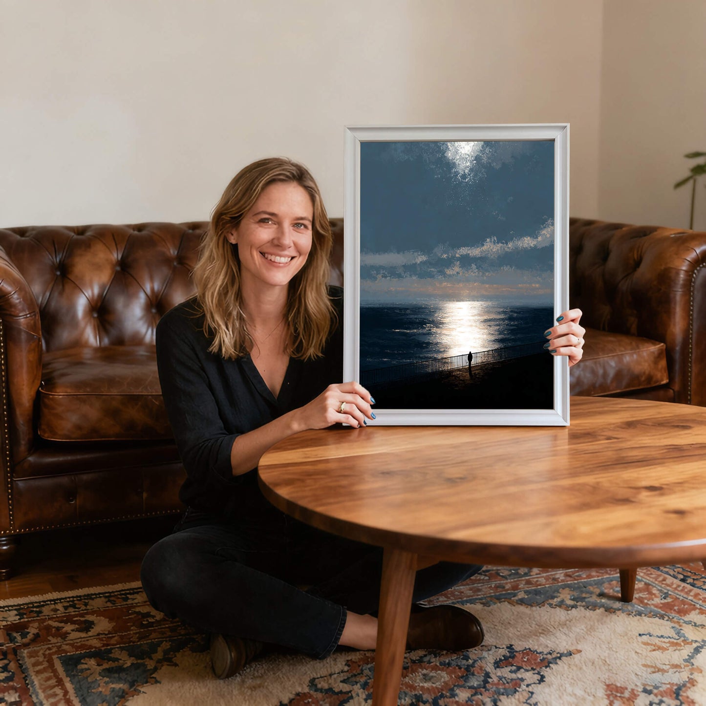 Smiling woman sitting on the floor holding the ocean sunset art print in a thin white wood frame, providing scale and showing the artwork's size relative to a person in a living room."
1 (10).jpg,